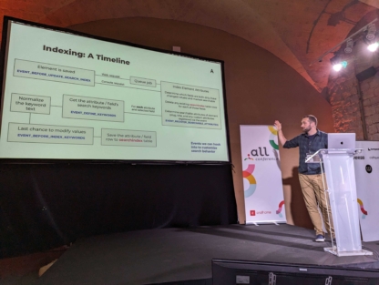 Gregor standing at the Dot All podium in front of a screen with information about search indexing.